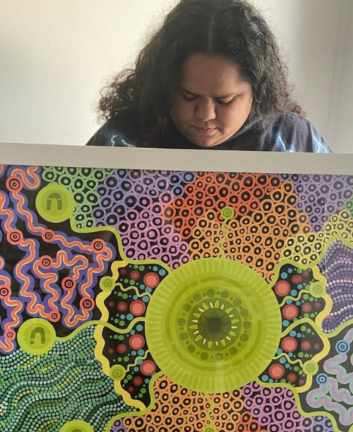 Alannah Brown holding one of her large circular Aboriginal artworks, smiling